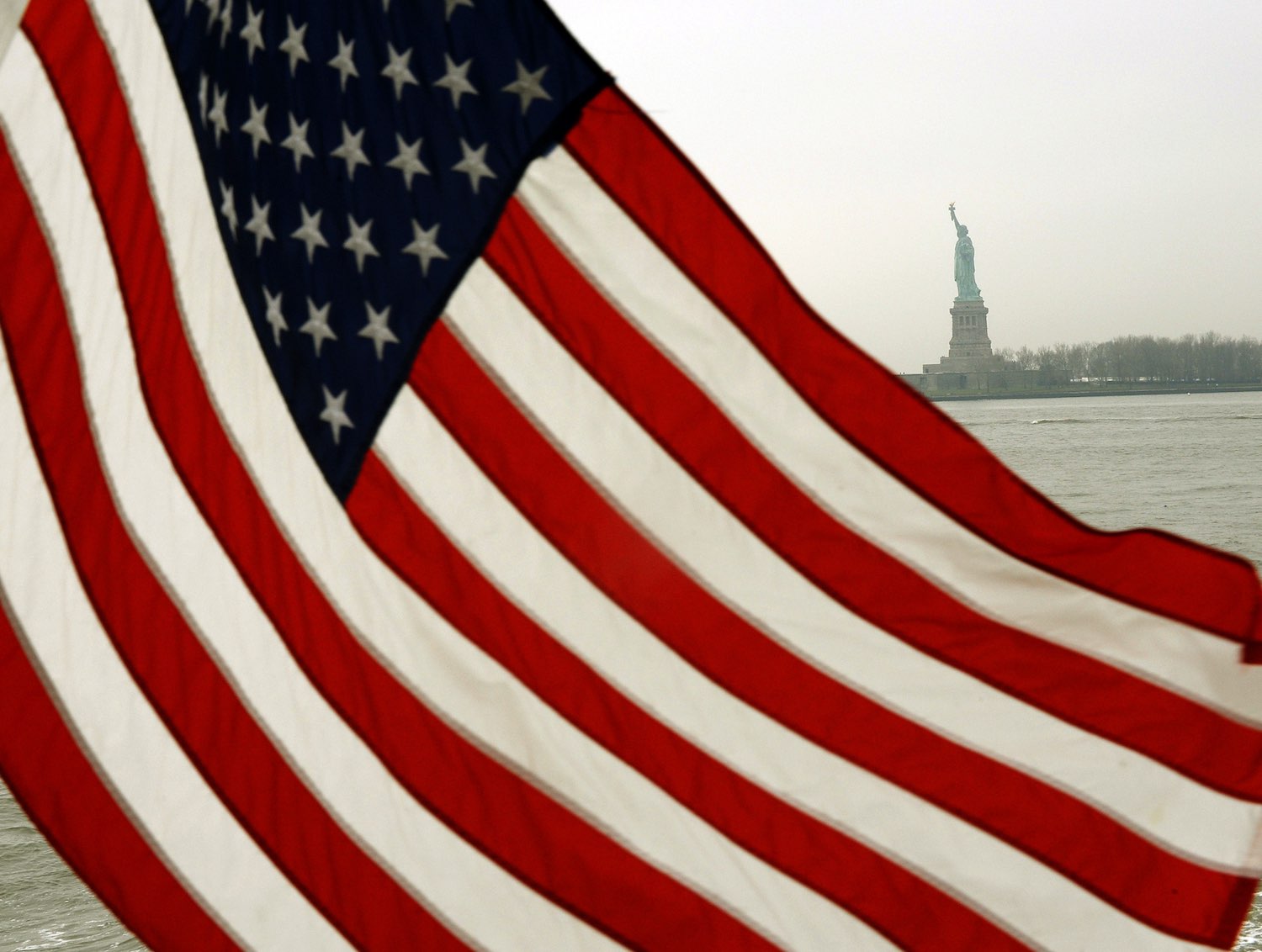 The U.S.A. national flag in the foreground, with the statue of liberty standing in the background.