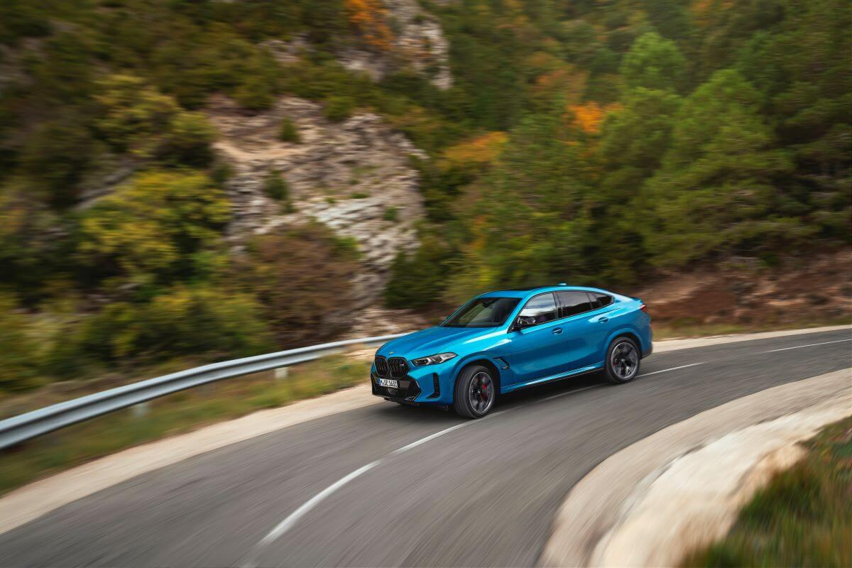 The new BMW X6 M60i xDrive midsize luxury SUV model driving on a curving country highway road