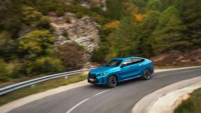 The new BMW X6 M60i xDrive midsize luxury SUV model driving on a curving country highway road