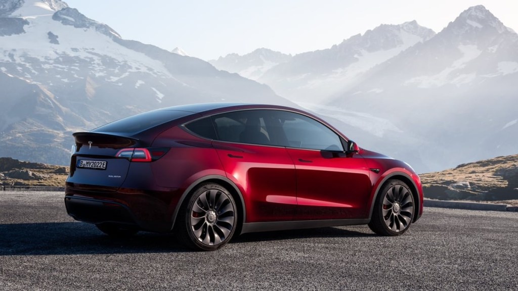 A red 2023 Tesla Model Y small electric SUV with mountains in background.
