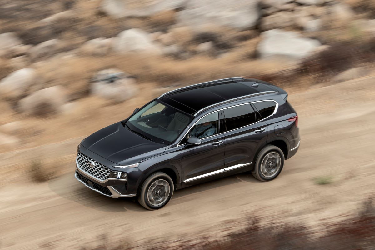An overhead shot of a 2023 Hyundai Santa Fe midsize SUV model driving through a desert with a blurred background