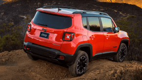 A rear shot of a 2023 Jeep Renegade compact crossover SUV model driving over a dirt hill in the wilderness