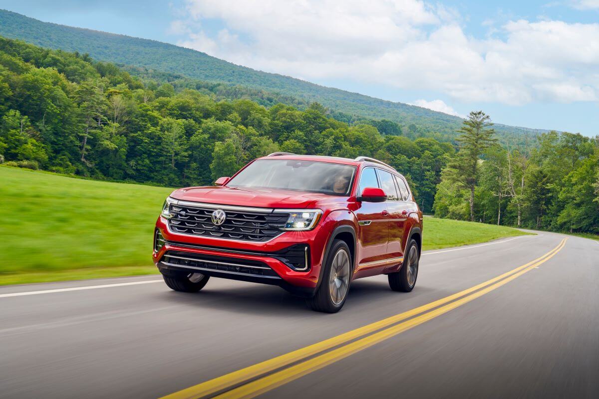 A 2024 Volkswagen Atlas three-row midsize SUV model in Aurora Red Metallic driving out of a green forest
