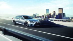 A 2024 Lexus ES midsize executive car/luxury sedan model driving on a highway overpass framed by a city skyline