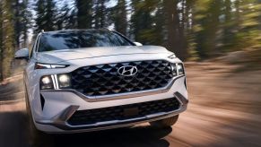 A closeup shot of the grille and headlights design on a white 2023 Hyundai Santa Fe driving in a forest