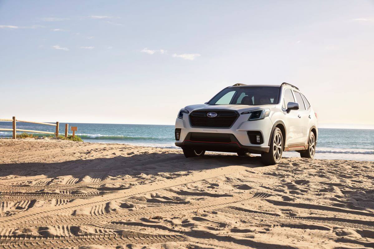A 2023 Subaru Forester compact crossover SUV model parked on a sandy beach covered in tire treads