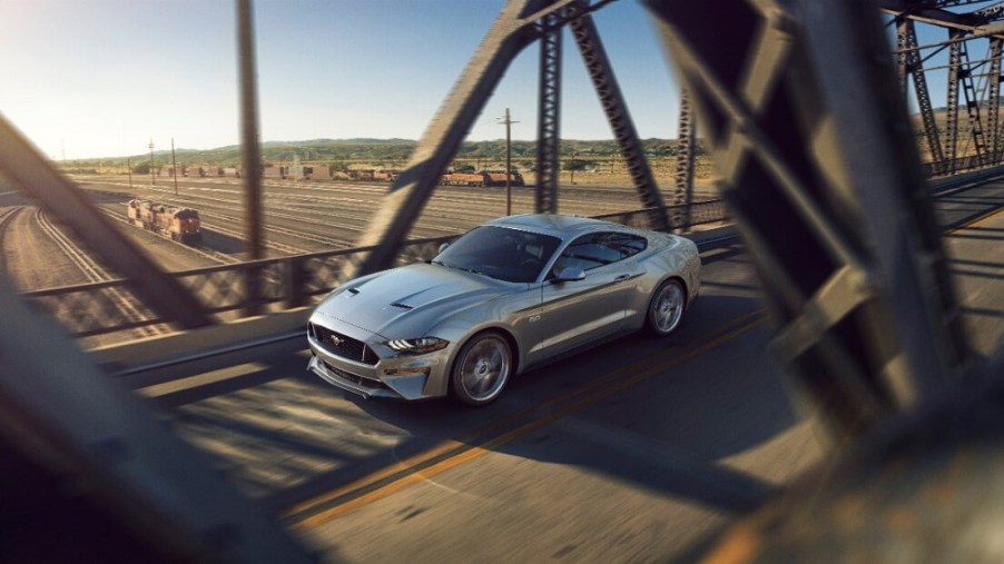 A silver S550 2023 Ford Mustang GT cruises on a city bridge.