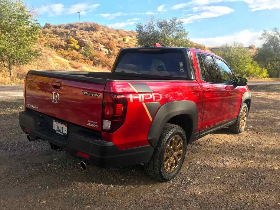 The tailgate of a red 2021 Honda Ridgeline sport with AWD parked in the woods.