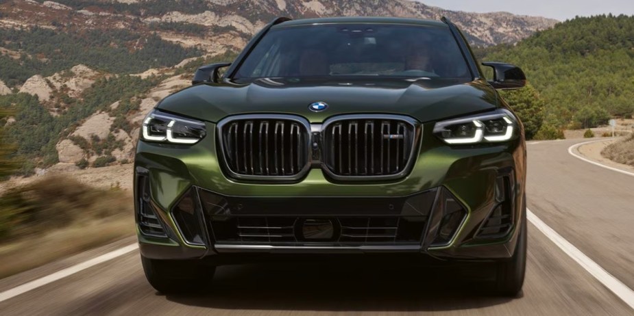 A green 2023 BMW X3 small luxury SUV is driving on the road. 
