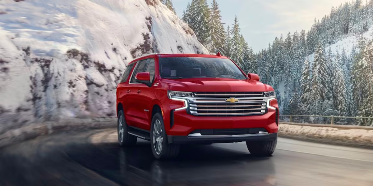 A red 2023 Chevrolet Suburban full-size SUV is driving on the road.