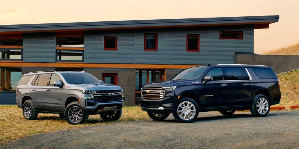 Two 2023 Chevrolet Suburban full-size SUVs are parked. Gray (L), Black (R).