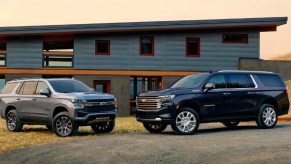 Two 2023 Chevrolet Suburban full-size SUVs are parked. Gray (L), Black (R).