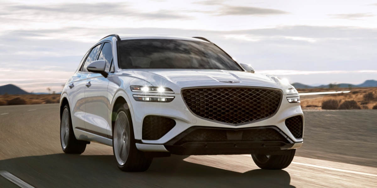 A white 2023 Genesis GV70 small luxury SUV is driving on the road.