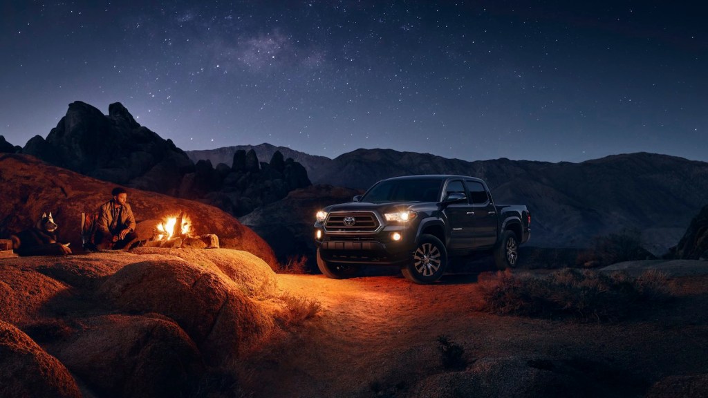 A 2023 Toyota Tacoma SR5 is parked off-road, with a campfire in the foreground.