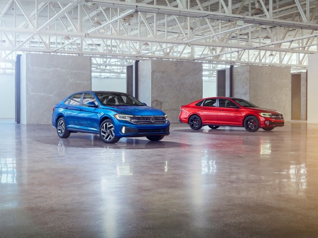 A set of blue and red 2023 Volkswagen Jetta show off their midsize car platforms in a warehouse.