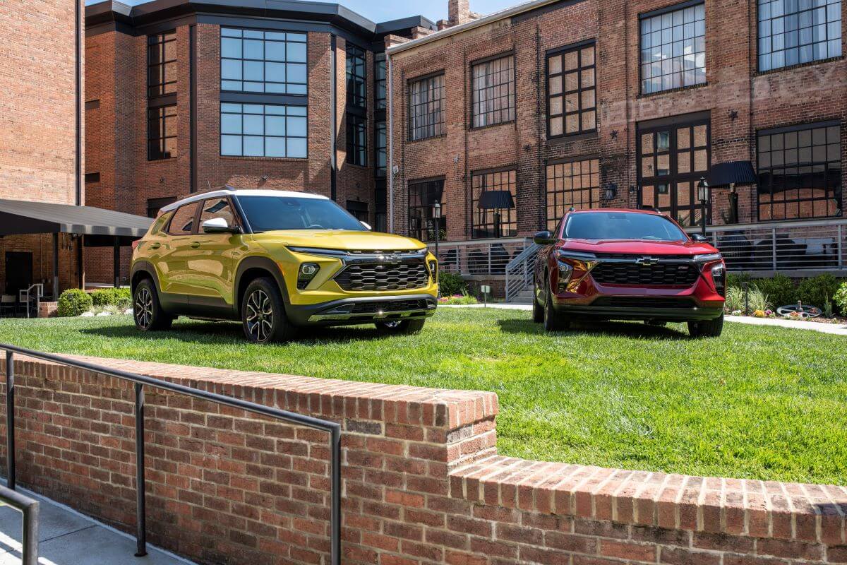 A 2024 Chevy Trax LT in Nitro Yellow (L) and 2024 Chevy Trax RS in Crimson Red (R) parked on a brick building plaza