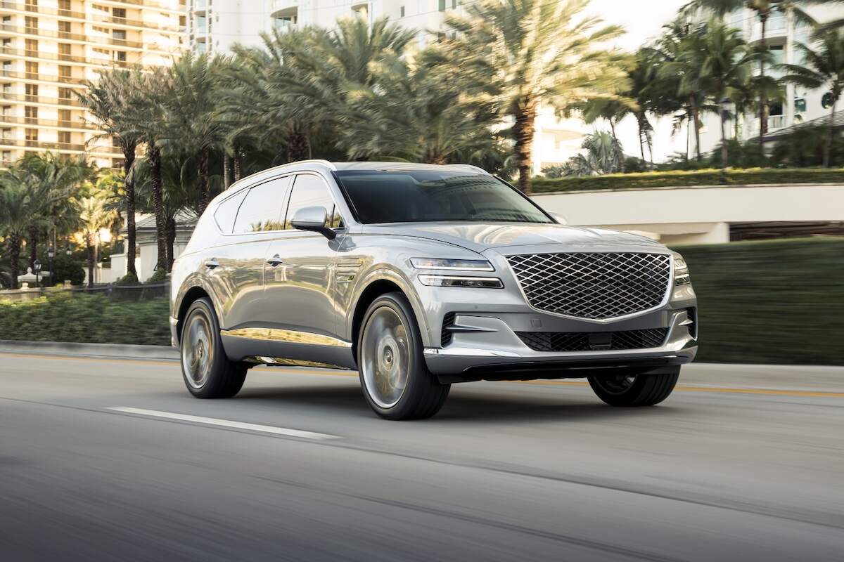 A silver 2024 Genesis GV80 drives past palm trees and high-rise condo buildings