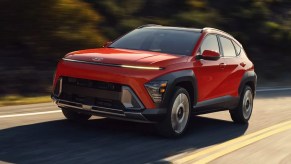 A red 2024 Hyundai Kona subcompact SUV is driving on the road.