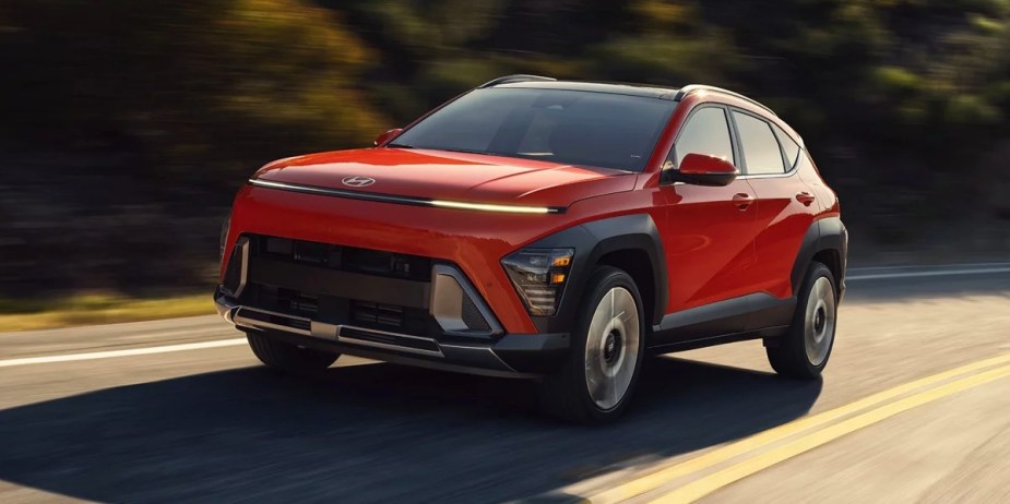 A red 2024 Hyundai Kona subcompact SUV is driving on the road. 