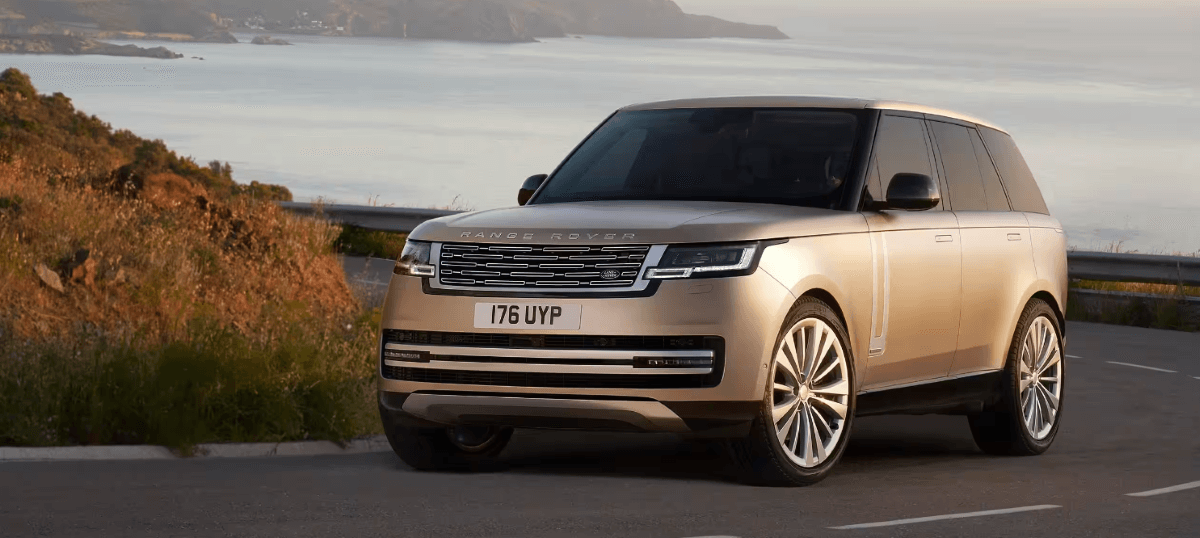 A 2024 Land Rover Range Rover 4x4 midsize luxury SUV model on a curving highway road overlooking the sea