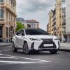 A white 2024 Lexus UX Hybrid taking a turn on a city street. The Lexus UX Hybrid price is one of its best selling points.