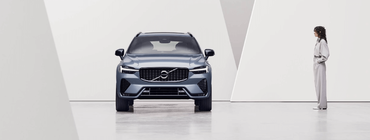 A promotional shot of a 2024 Volvo XC60 compact luxury SUV model as a woman stares at its profile
