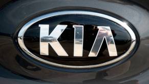 A silver Kia logo on the front of a car.