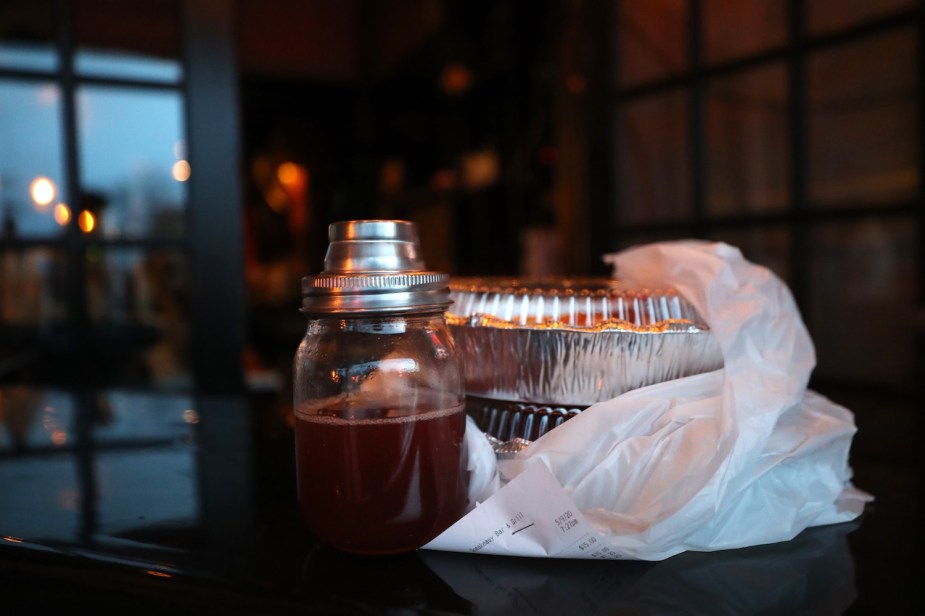 A meal and a cocktail packaged to go on the counter of a sports bar in Rhode Island, a window visible in the background.