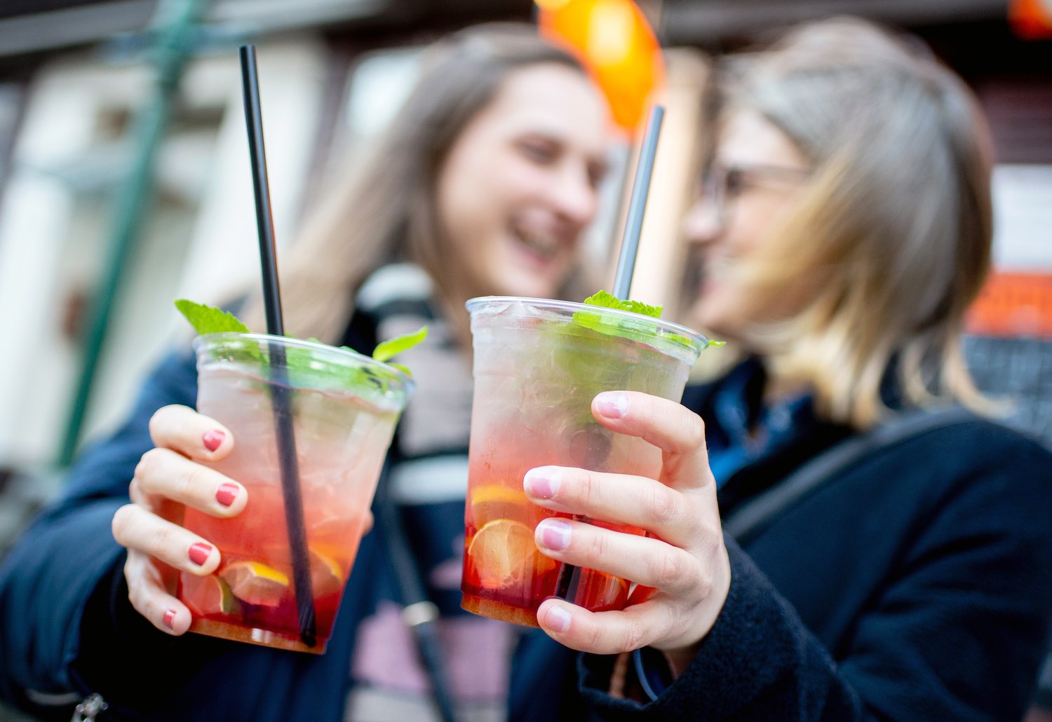 Two women toast with alcoholic cocktails to go.