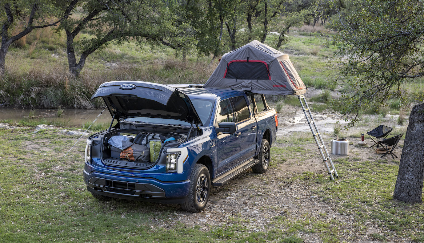 A blue Ford F-150 Lightning using its frunk at a campsite. The F-150 Lightning's price cuts raises interesting questions