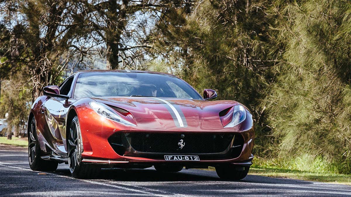 Ferrari 812 Superfast coupe driving on public road with italian flag racing stripes