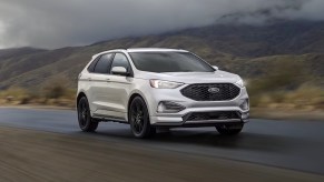 A white Ford Edge midsize SUV is driving on the road.