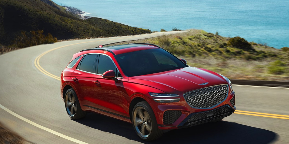 A red 2023 Genesis GV70 small luxury SUV is driving on the road.