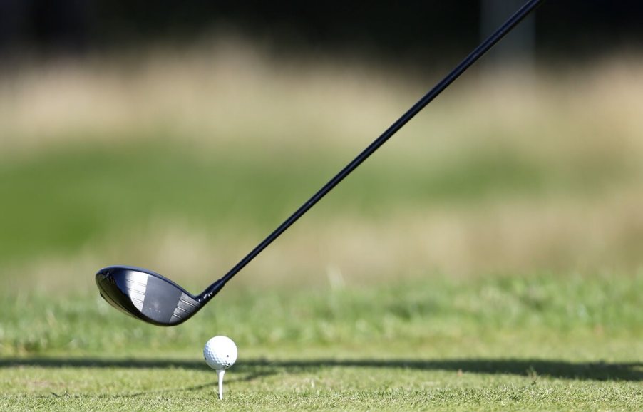 A golf club lines up a shot next to a ball on a tee.