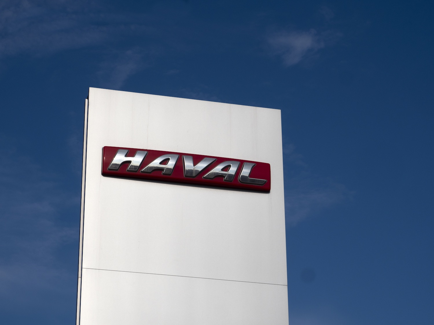 The Haval logo on a sign above a dealership, a blue sky in the background.
