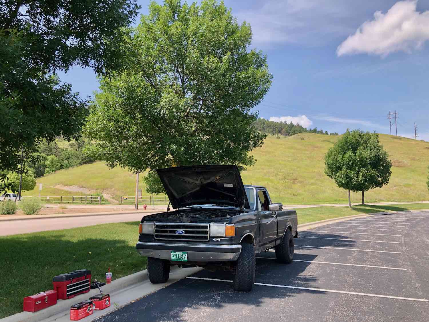This is Henry Cesari's black 1988 Ford F-150 in a parking lot with its hood up for repairs it's an example of an 80s and 90s truck.