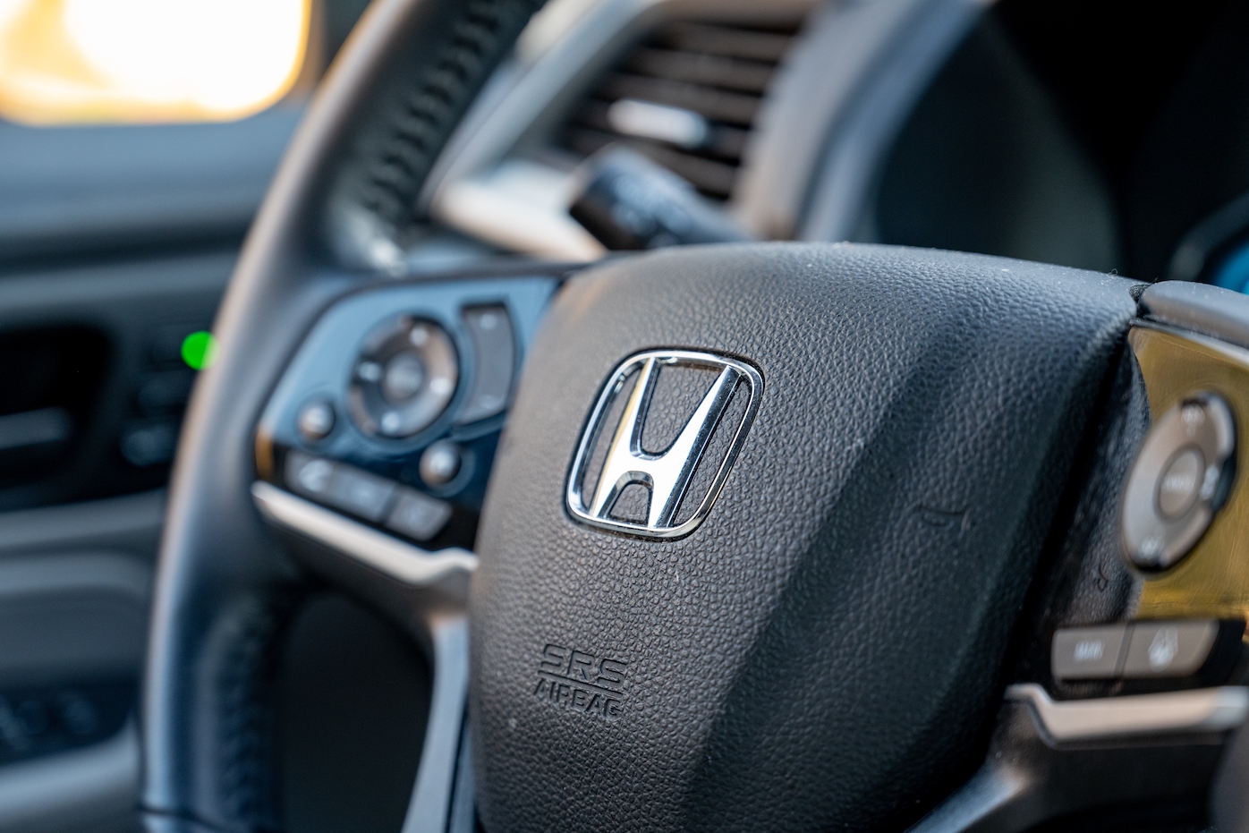 Close-up of Honda logo on steering wheel of a vehicle, with vehicle interior visible. Honda sales have made these models more popular