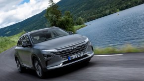A gray Hyundai Nexo driving next to a lake by a mountain. The Hyundai Nexo hydrogen fuel cell complicates fueling.