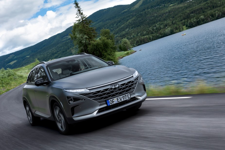 A gray Hyundai Nexo driving next to a lake by a mountain. The Hyundai Nexo hydrogen fuel cell complicates fueling.