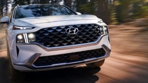 A white 2023 Hyundai Santa Fe midsize SUV is driving on the road.