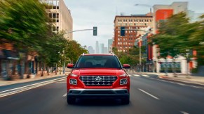 A red 2023 Hyundai Venue subcompact SUV is driving on the road.