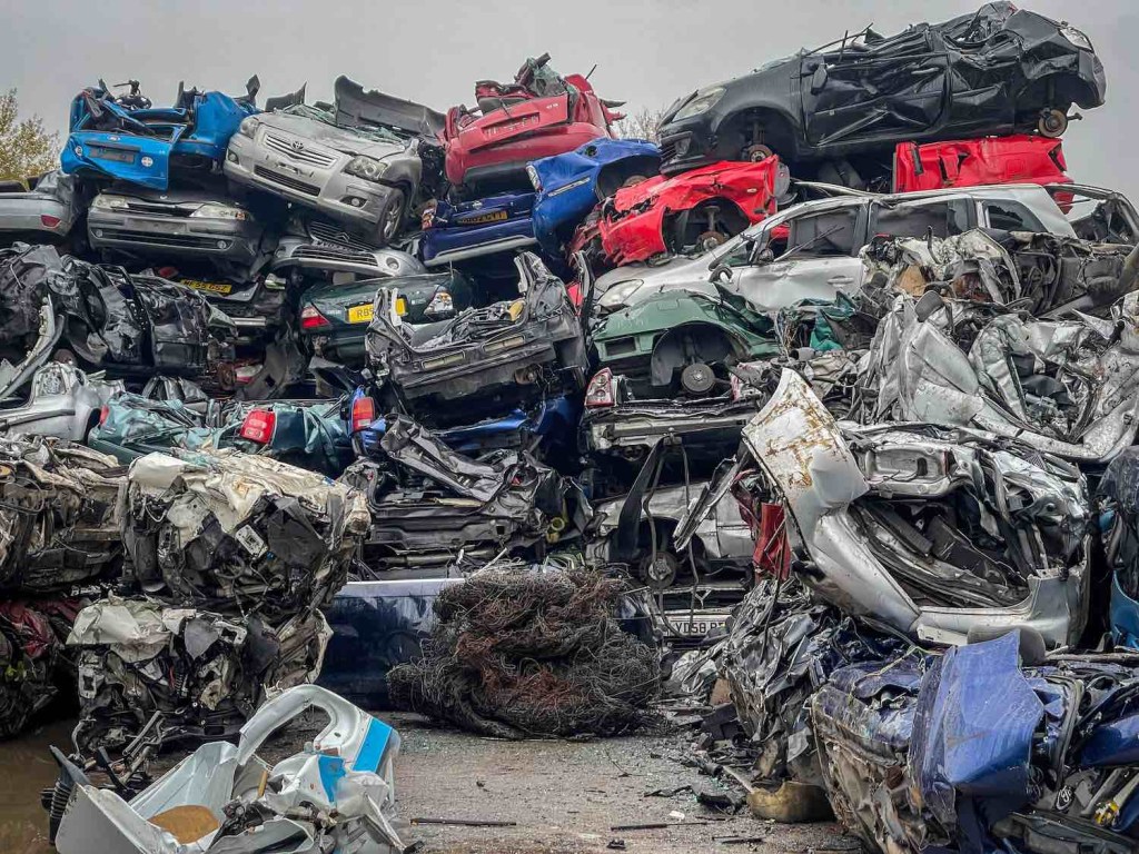 A pile of internal combustion cars in a scrapyard to be replaced by electric vehicles.