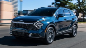 A blue 2023 Kia Sportage Hybrid small hybrid SUV is driving on the road.