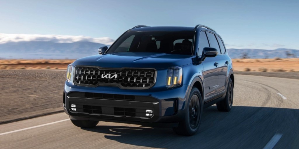 A blue 2024 Kia Telluride is driving on the road.