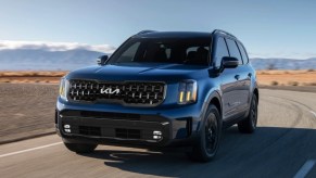 A blue 2024 Kia Telluride is driving on the road.