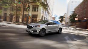 A silver Ford Edge taking a turn on a city road. The last Ford Edge comes in 2024 before the model fades out of production.