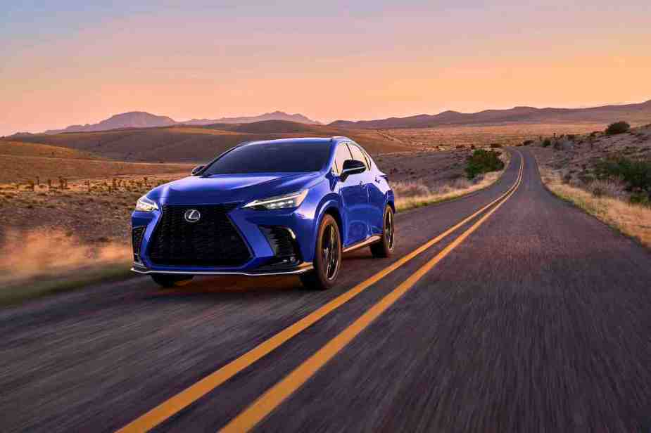 A blue 2024 Lexus NX 450h driving along a desert road at sunset. This is one of the Lexus Hybrid SUVs that falls short to the Porsche Cayenne.