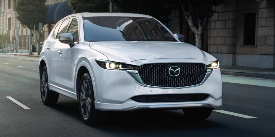 A white 2024 Mazda CX-5 small SUV is driving on the road, it's an excellent daily driver.