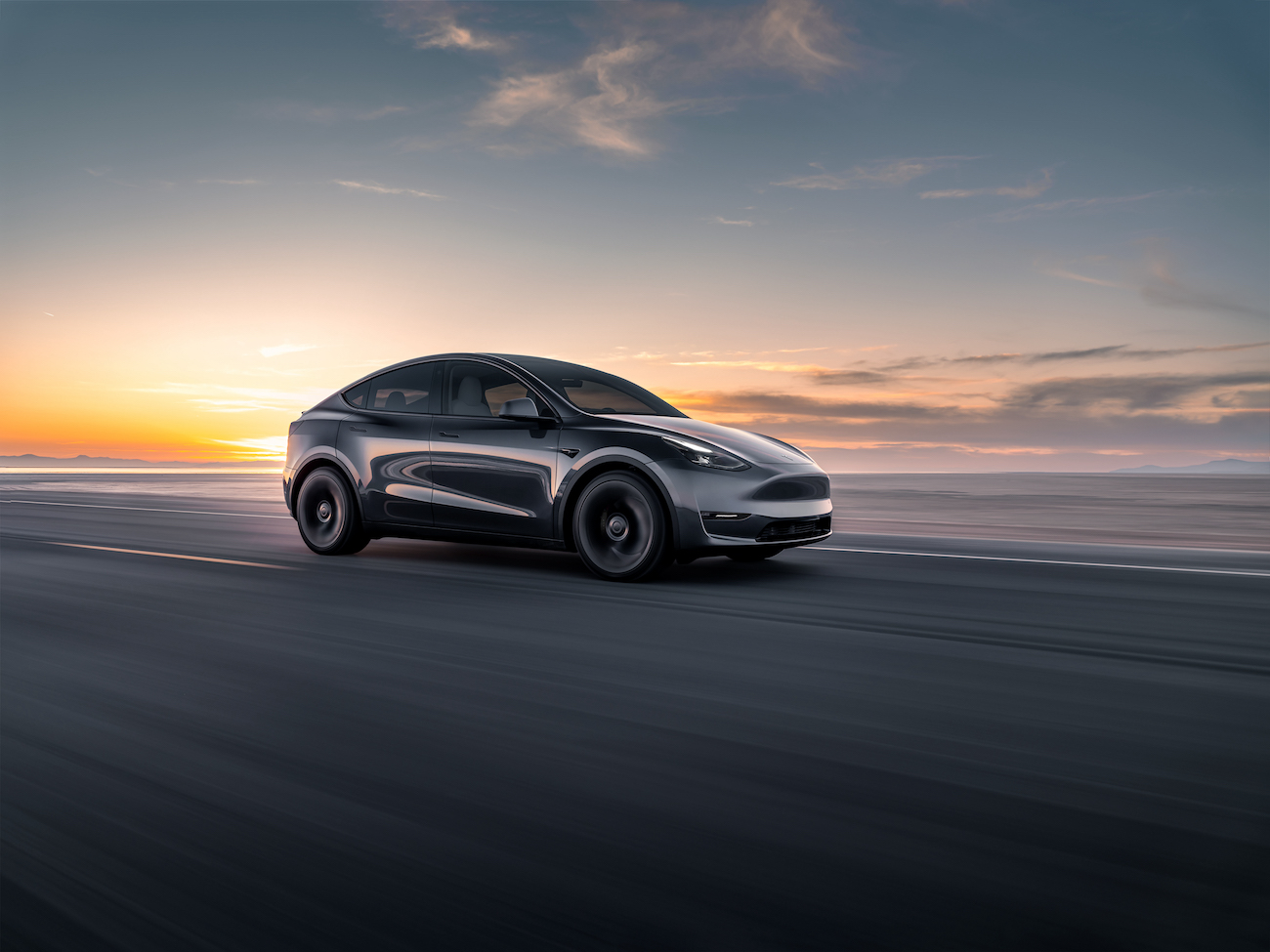 A black Tesla Model Y driving at sunrise. EV prices for the Model Y finally are on the way down