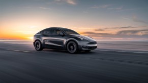 A black Tesla Model Y driving at sunrise. EV prices for the Model Y finally are on the way down